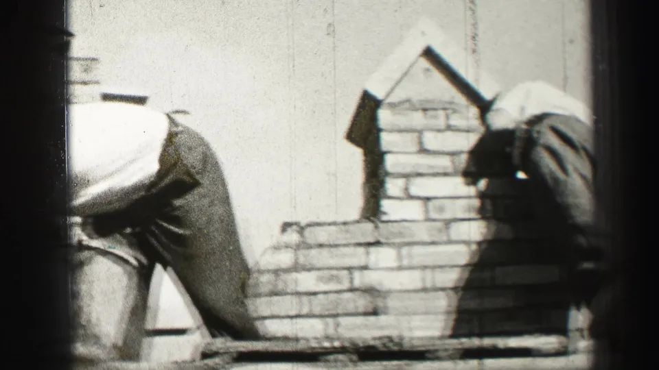 The final frame shows two adult workers bending around the partly built rooftop chimney in grainy 1952 Scotland home-movie footage.