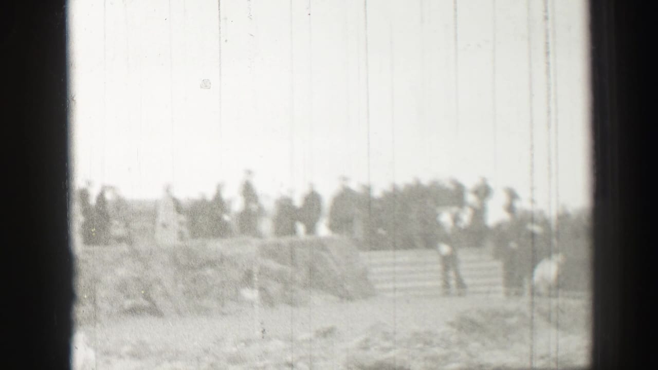 Grainy 1952 Scotland home-movie frame showing people gathered on stone steps near rough stonework.