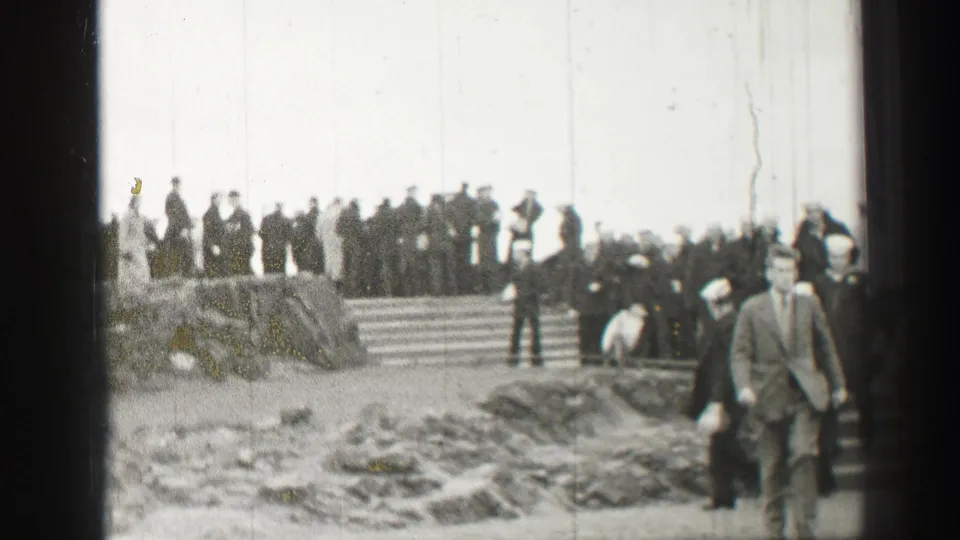Black-and-white 1952 Scotland frame with uniformed personnel and civilians gathered around outdoor stone steps.