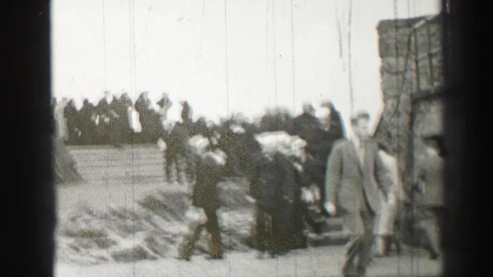 1952 Scotland home-movie frame showing civilians and uniformed figures walking near stone steps and masonry.