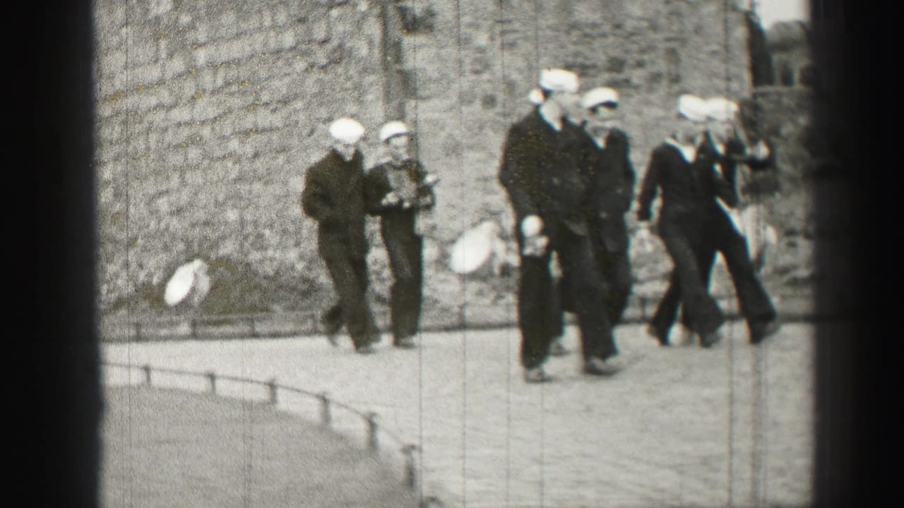 In 1952 Edinburgh footage, sailors in white caps and dark uniforms walk near a weathered stone building as the frame edges show 8mm film artifacts.