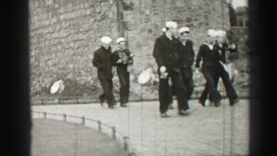 In 1952 Edinburgh footage, sailors in white caps and dark uniforms walk near a weathered stone building as the frame edges show 8mm film artifacts.