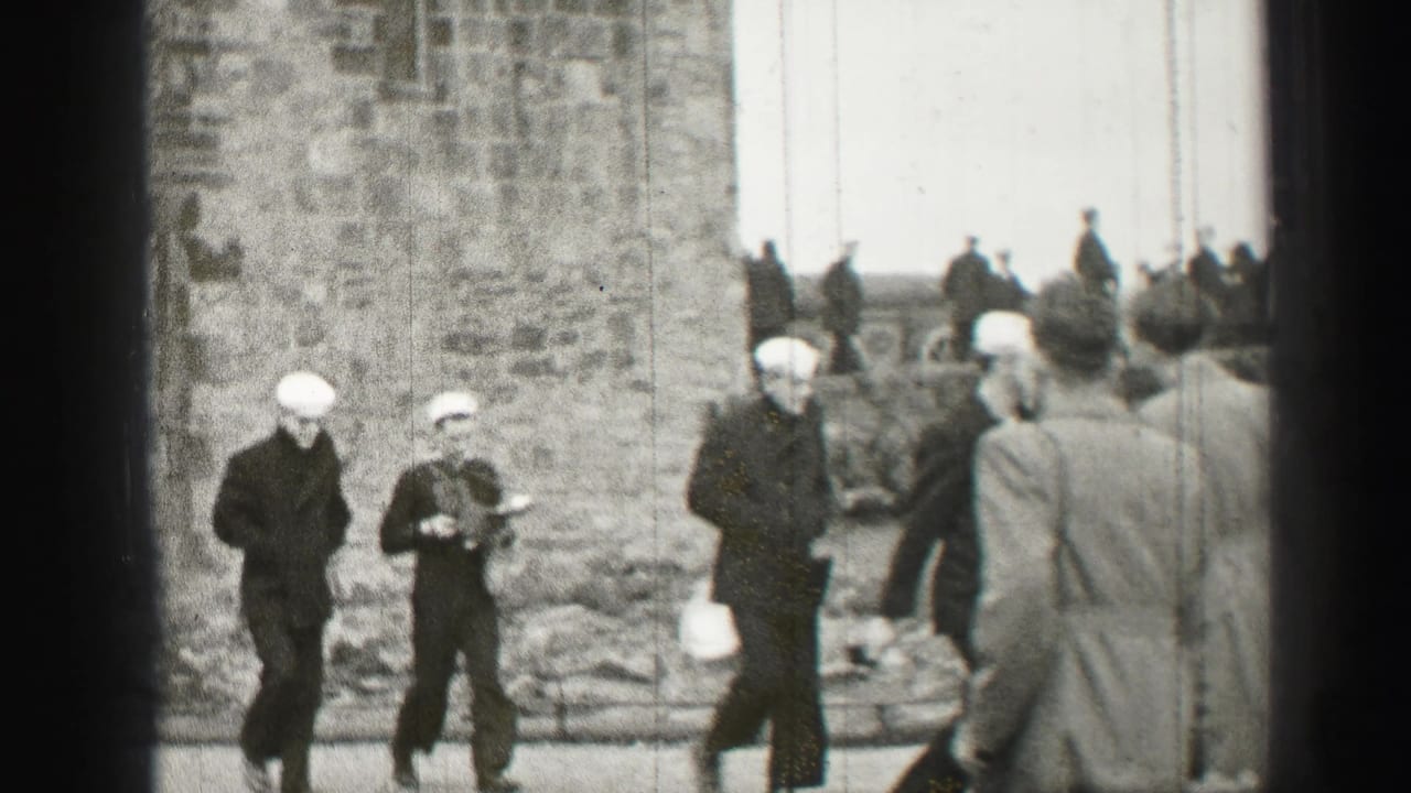 Uniformed sailors in white caps move near a rough stone wall in Edinburgh, with civilians and steps visible in the background.