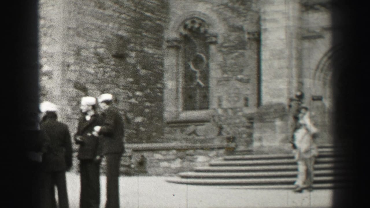 Men in hats and suits stand outside a stone cathedral facade near steps and a stained glass window.