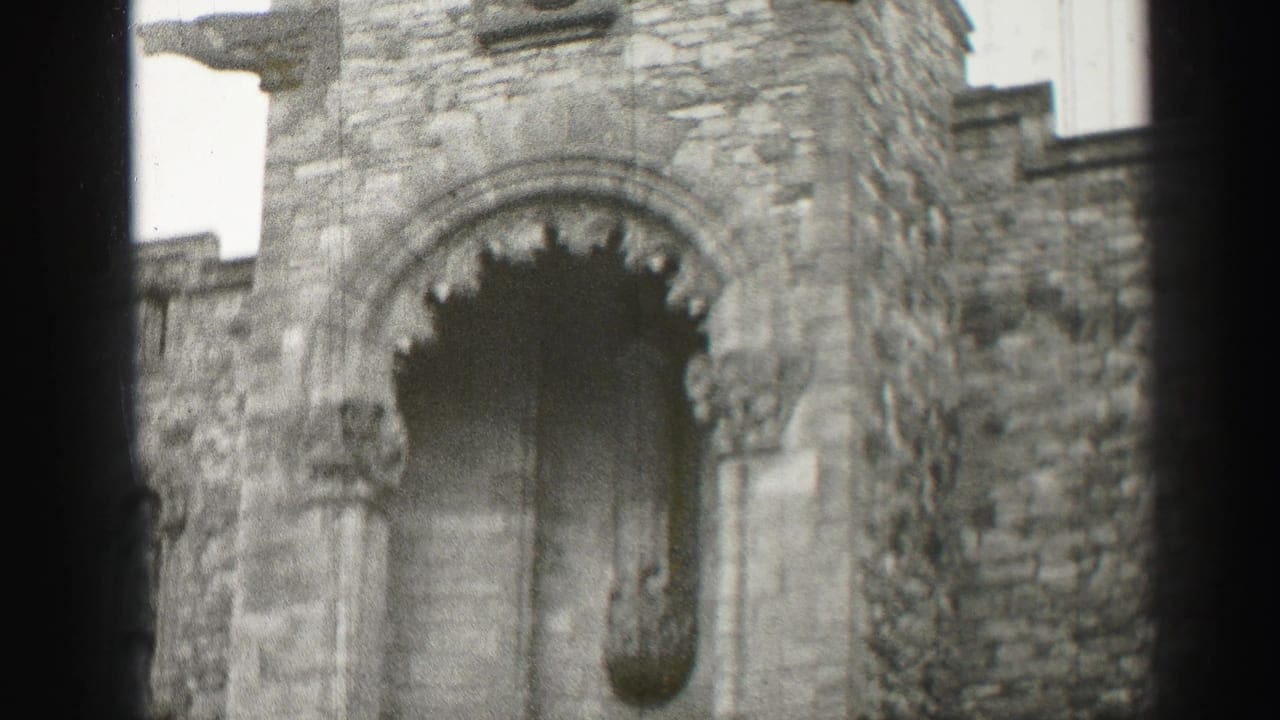 1952 home-movie frame from Edinburgh showing a close view of a stone Romanesque-style facade with an arched opening and carved details.