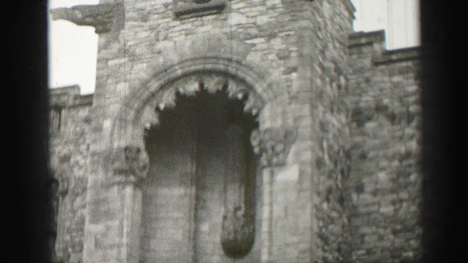 1952 home-movie frame from Edinburgh showing a close view of a stone Romanesque-style facade with an arched opening and carved details.