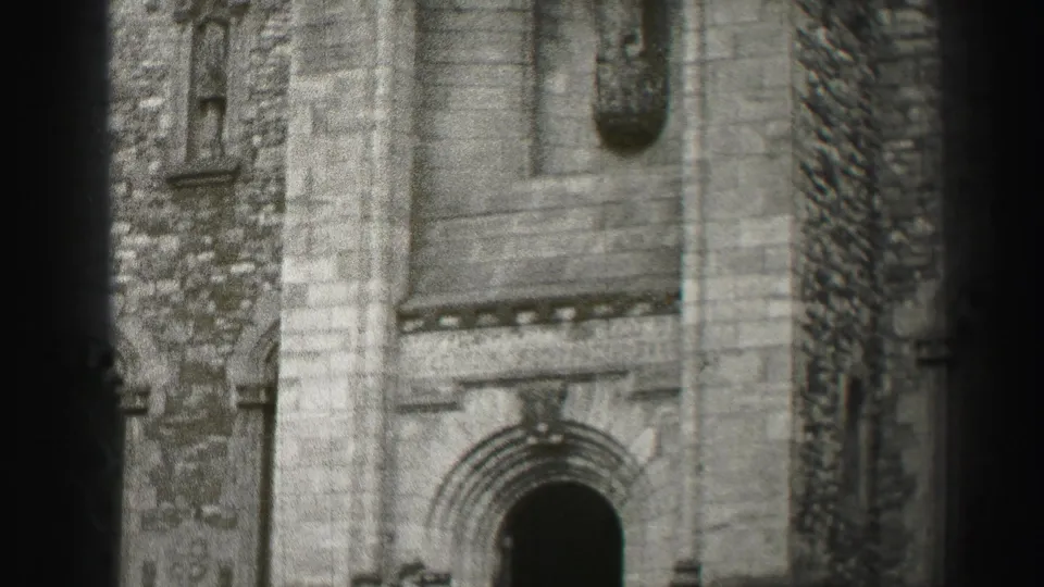 Black-and-white 8mm frame of a historic stone church facade in Edinburgh, with an arched doorway partly obscured by film-edge bands.