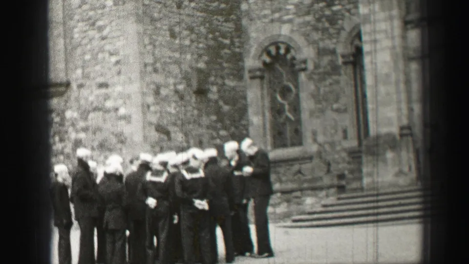 Uniformed sailors appear gathered in a solemn group outside a stone church in Scotland, based on the clip metadata.