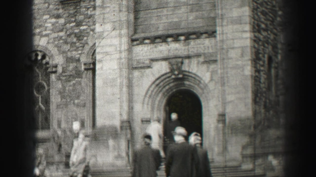 1952 Edinburgh home-movie frame showing adults in winter coats near a stone church entrance and arched doorway.
