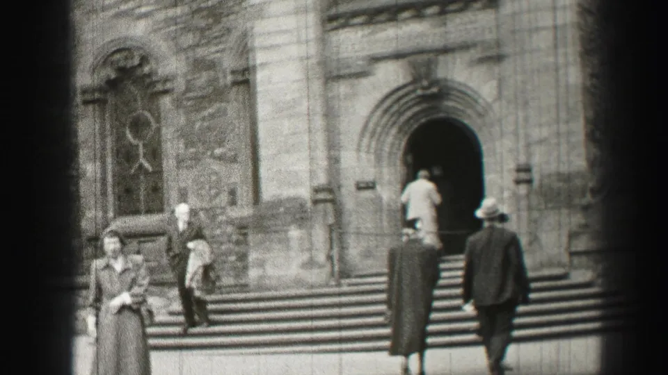 Adults in mid-century coats and hats climb the steps of an Edinburgh church exterior in black-and-white 8mm footage.