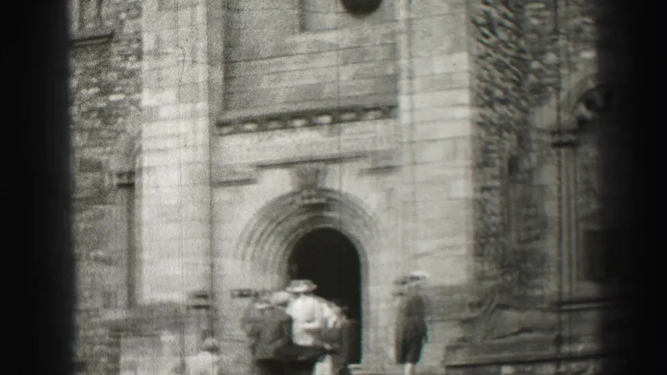 Adults in mid-century formal clothing stand and move near a recessed arched entrance in the Edinburgh 1952 clip.