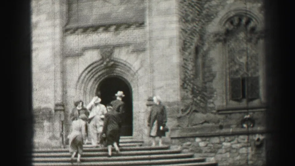 The 1952 Edinburgh home-movie frame shows visitors climbing steps beside a Gothic-style stone facade and arched doorway.