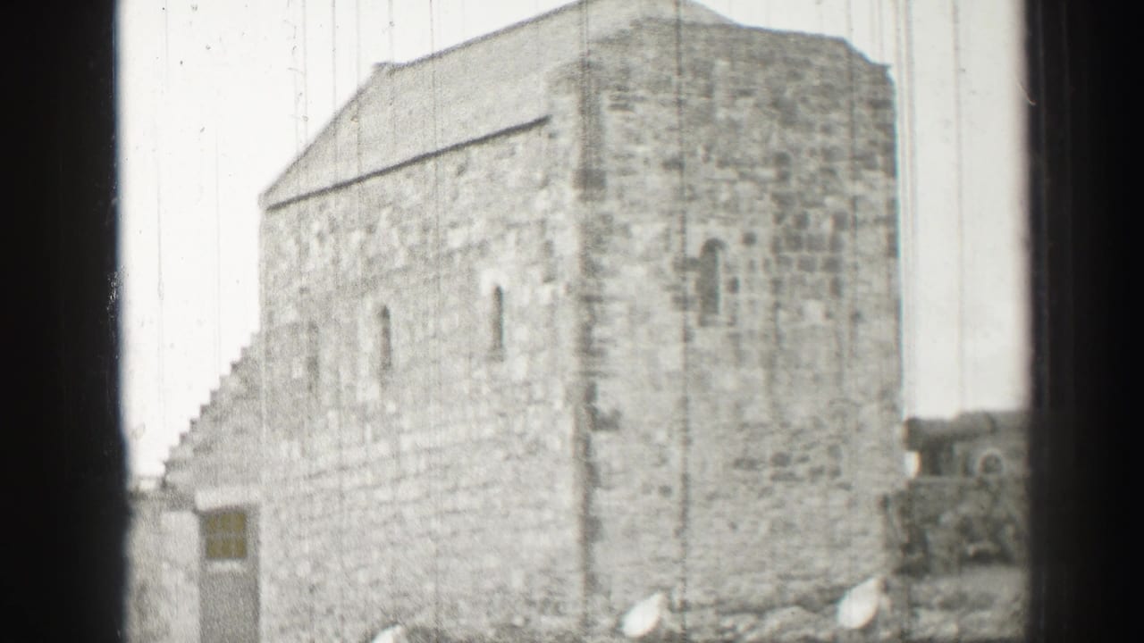 A broad exterior wall of an old stone building appears in soft black-and-white 8mm footage.