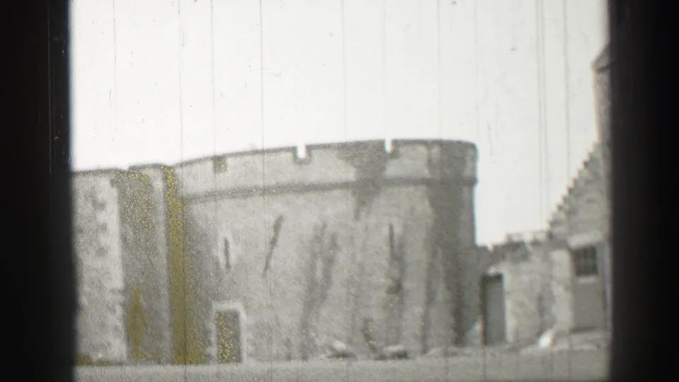 1952 8mm view of a stone castle tower and battlements in Edinburgh, framed by dark gate edges and film wear.