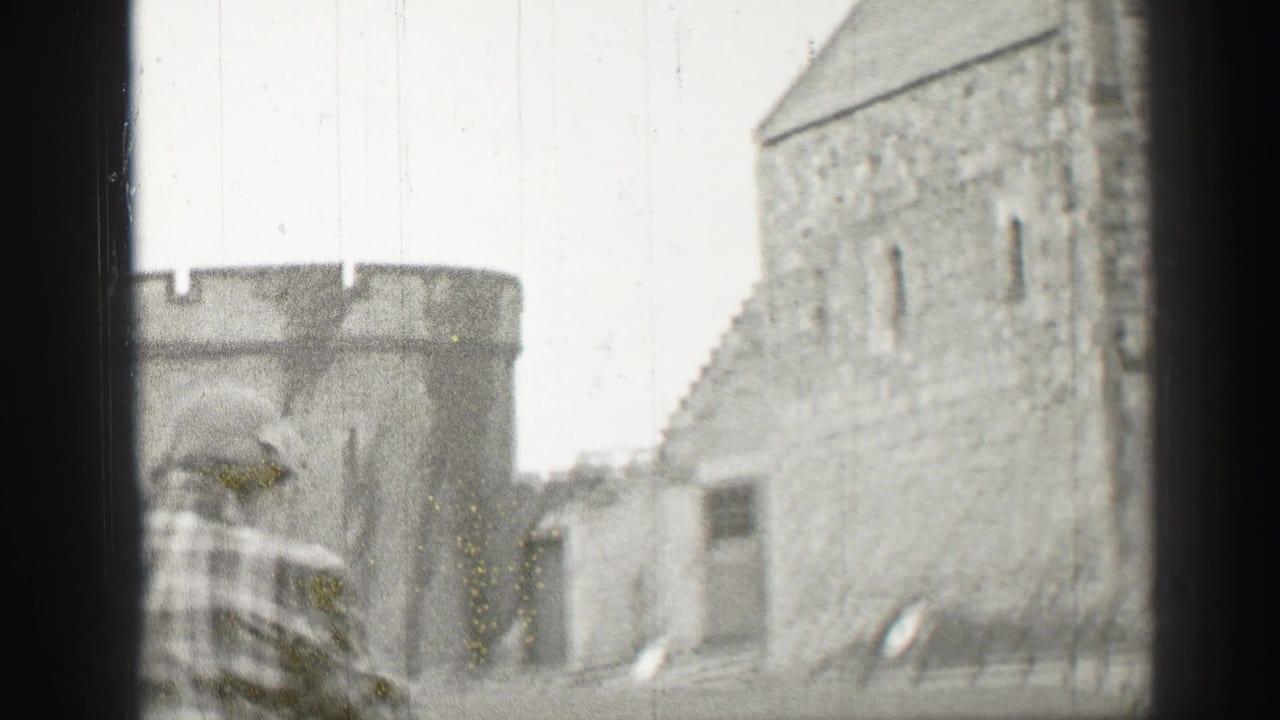 Kilted man standing near stone castle buildings and battlements.