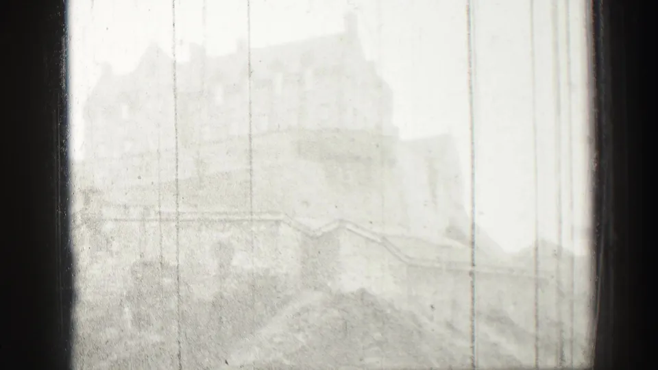 Soft, overexposed 8mm frame showing distant Edinburgh castle masonry and sloping stone forms through scratches and gate edges.