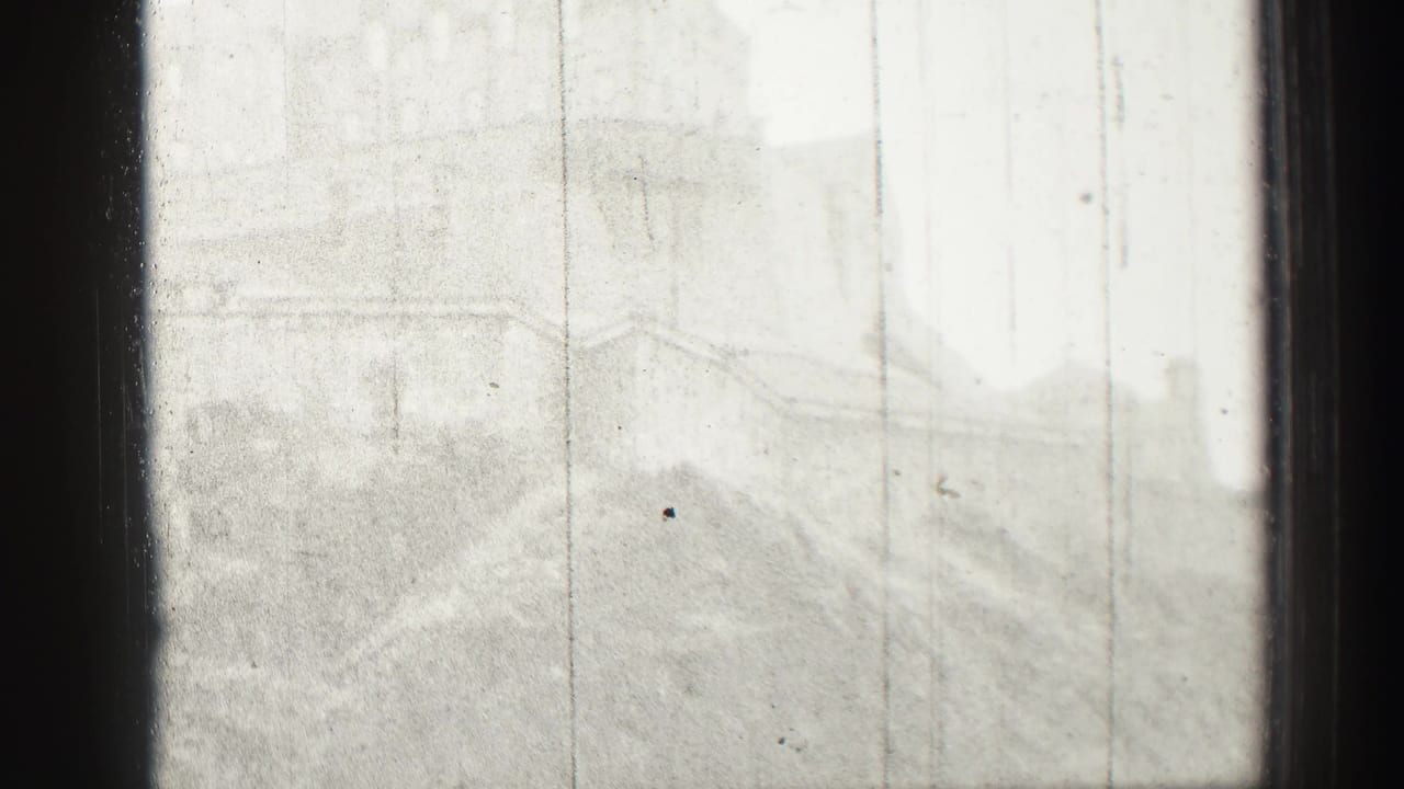 Distant Edinburgh Castle and hillside appear faintly through haze, scratches, and dark vertical window framing in this 1952 8mm frame.