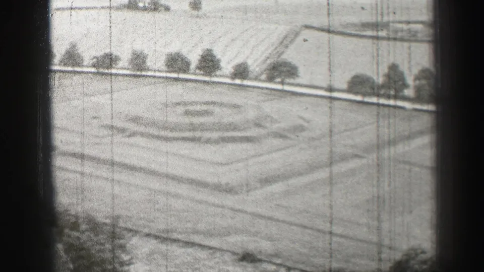 1952 Edinburgh home-movie frame showing an elevated view over geometric lawn patterns, paths, and a tree-lined edge.