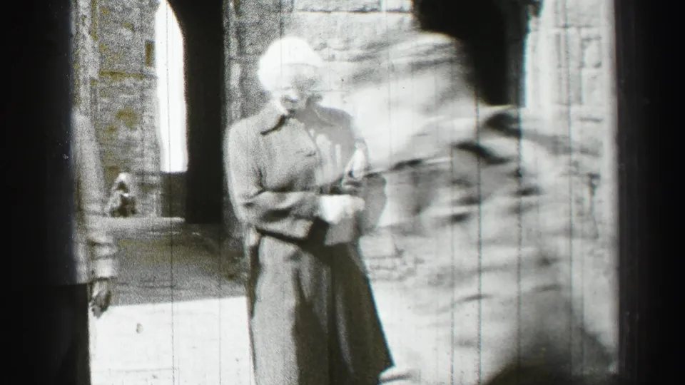 1952 Edinburgh home-movie frame showing adults walking near a stone building entrance, with faces indistinct and motion blur.