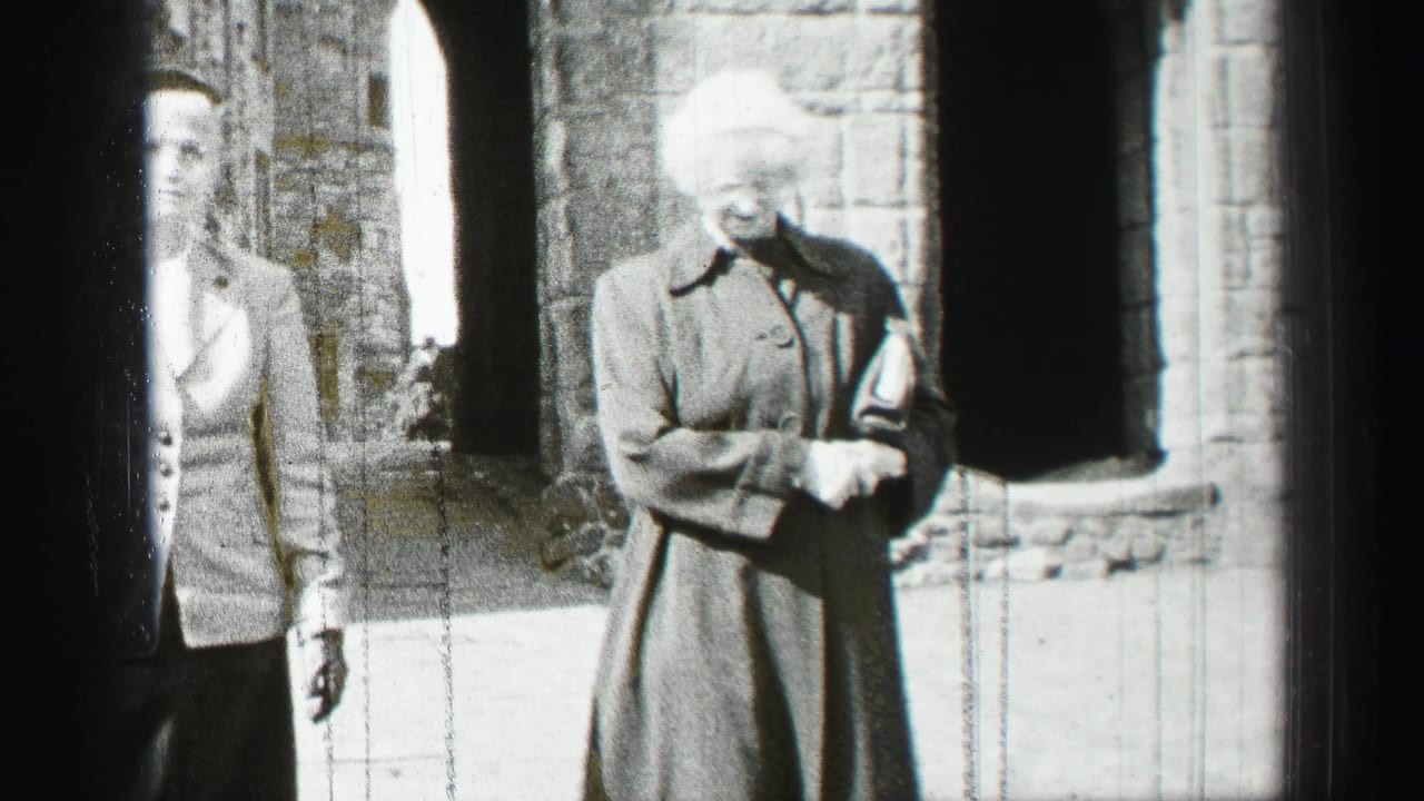Two women in 1950s-style coats and hats walk through a stone courtyard in Scotland, with arched openings behind them.