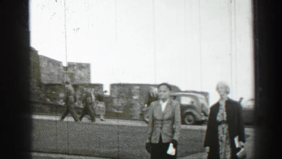 1952 Edinburgh street view with pedestrians in mid-century clothing walking near parked cars and stone buildings.