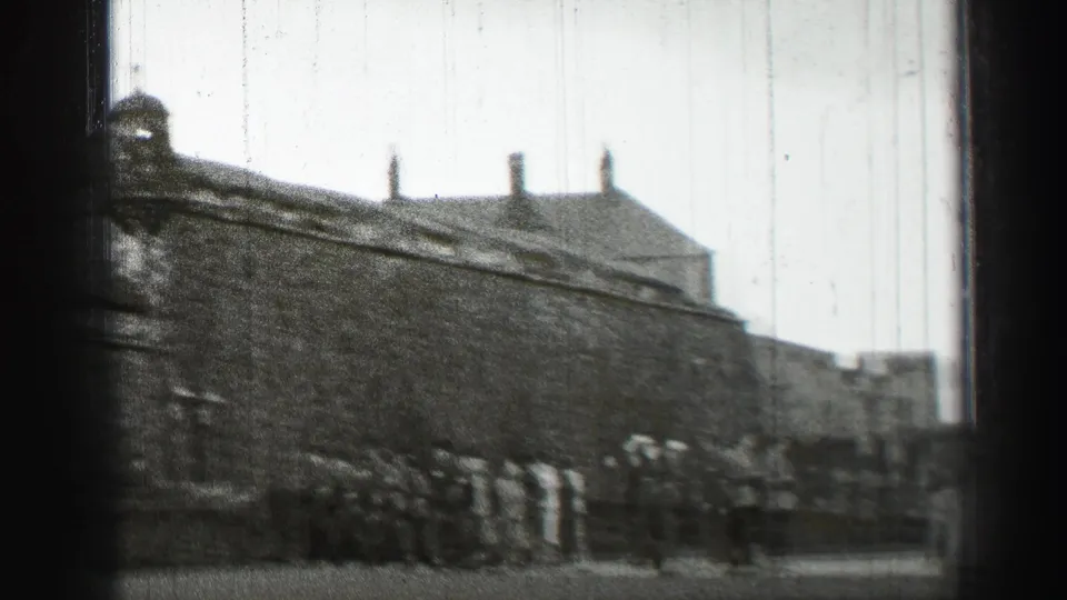 Edinburgh streetscape with a long stone wall, rooftops, and people gathered or walking in the distance.