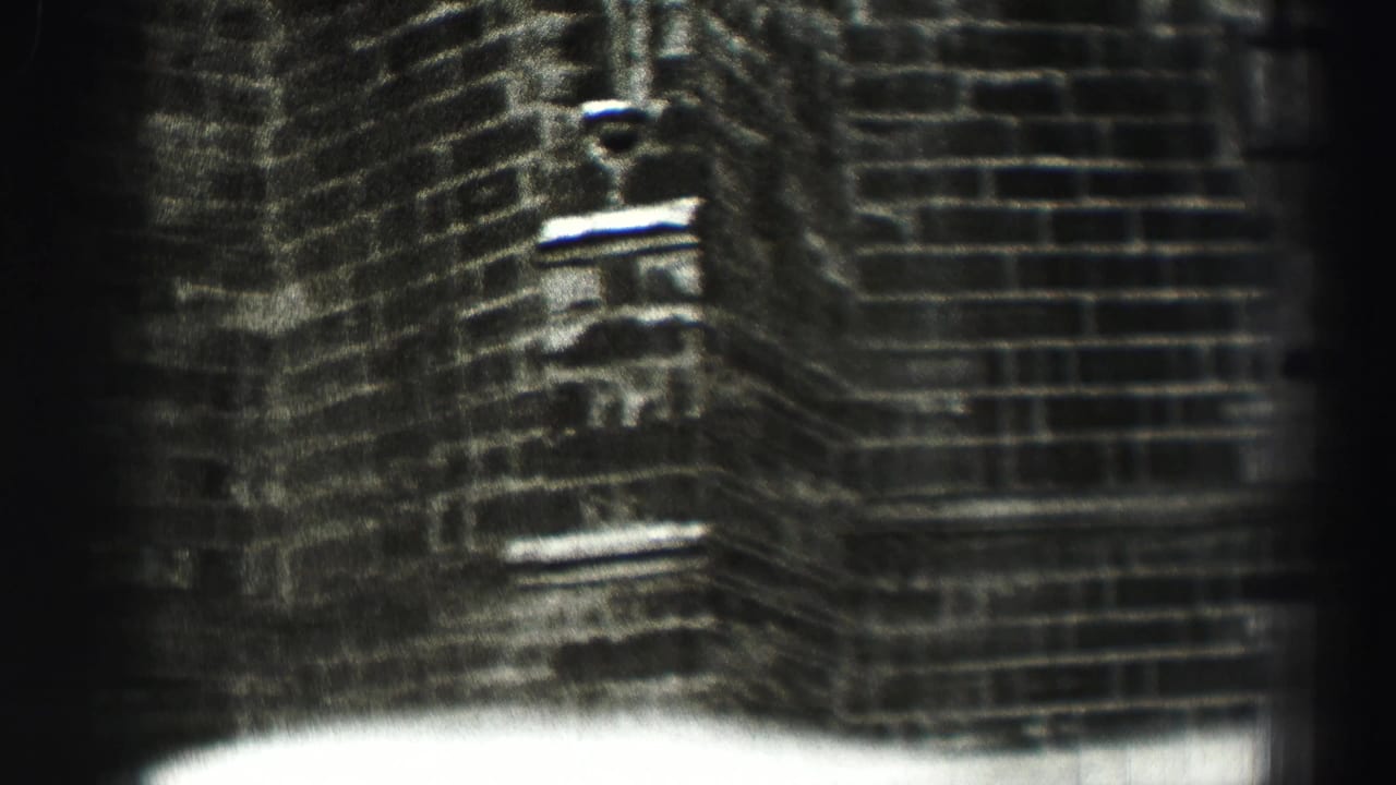 Soft monochrome close-up of a brick building corner with small openings and dark film edges.