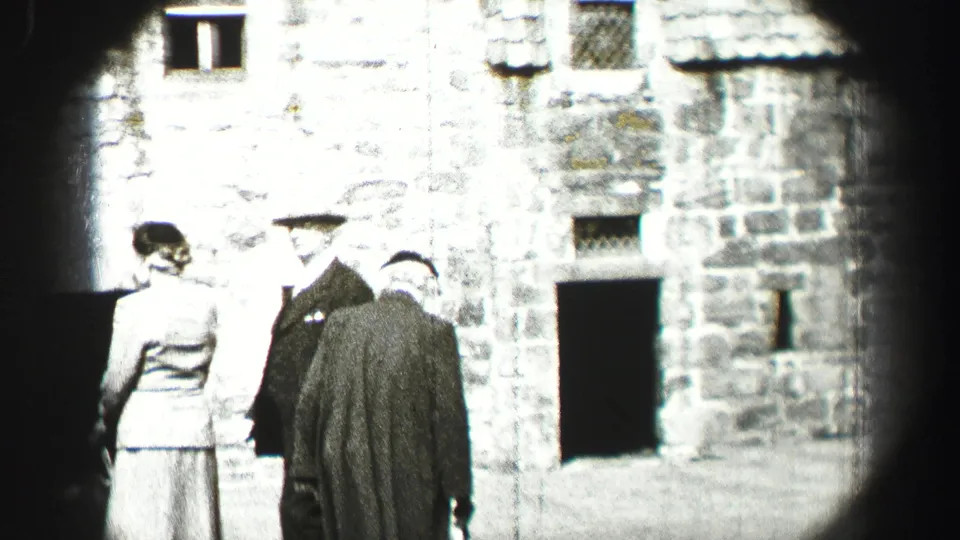 In 1952 Edinburgh, Scotland, well-dressed adults stand near small windows and dark openings in a stone facade.
