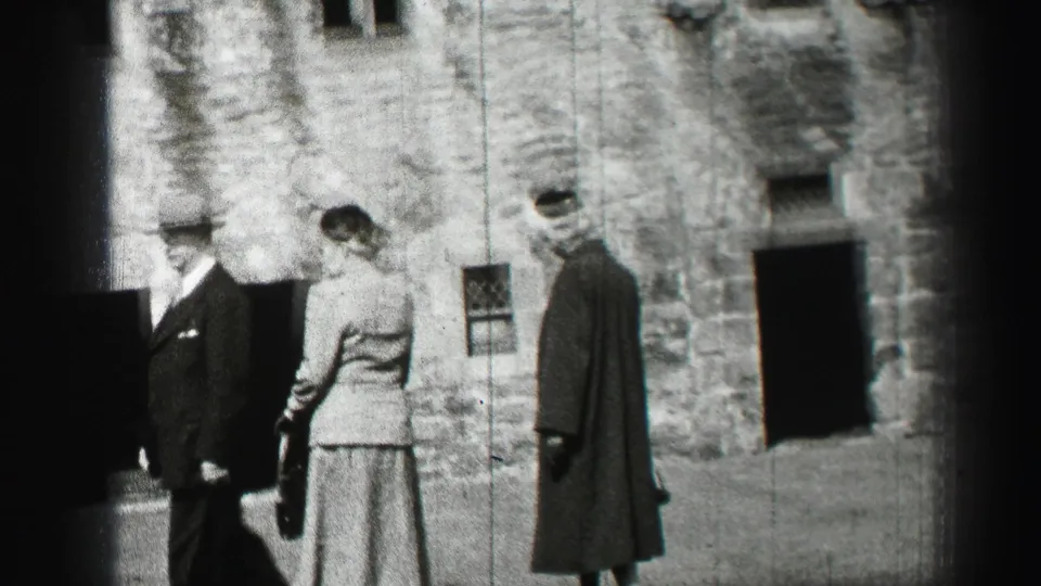 A suited man and two formally dressed women stand outside a stone building in the 1952 Edinburgh home-movie footage.