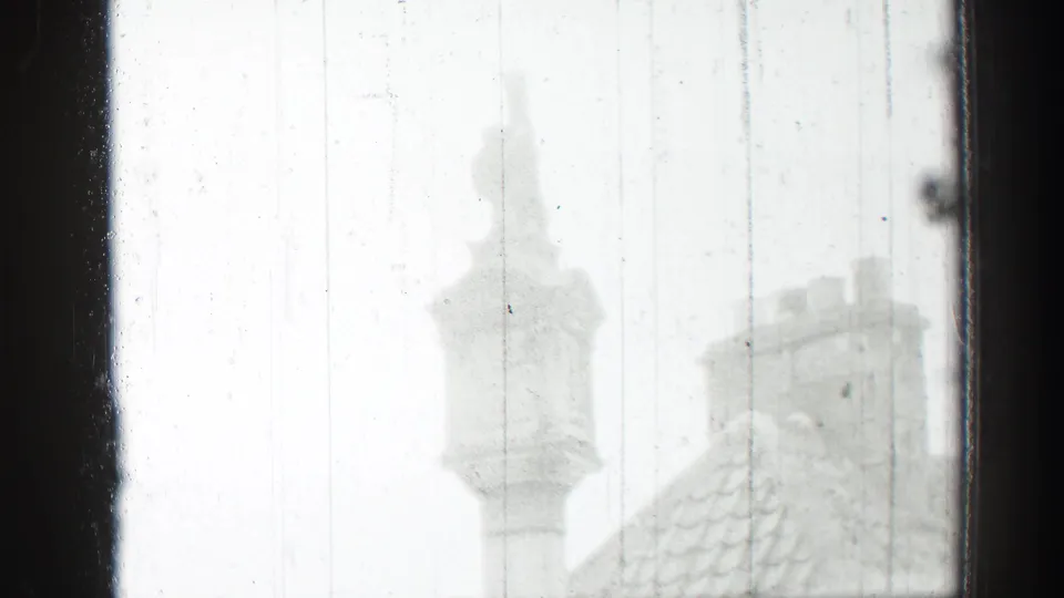 1952 8mm Edinburgh view through rain-marked glass, with tiled roofs and pale chimneys softened by exposure and focus.