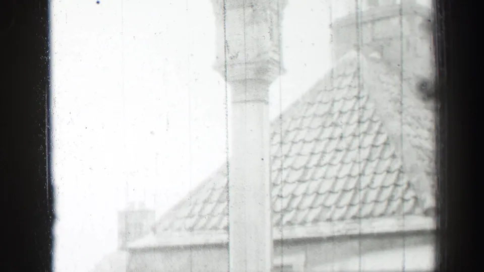 1952 Edinburgh rooftop detail seen through rain-streaked window glass, with a tiled roof and pale chimney shapes.