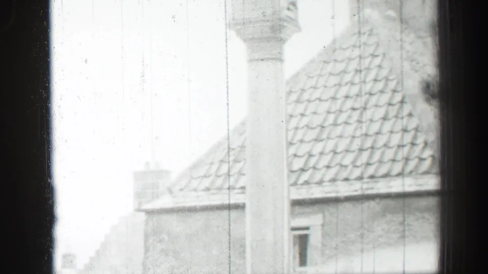 1952 Edinburgh home-movie frame looking through a window at stone houses, roof tiles and a prominent column.