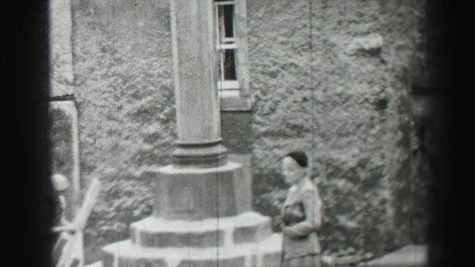 1952 Edinburgh home-movie frame showing a woman by a column outside a stone building with a window behind her.