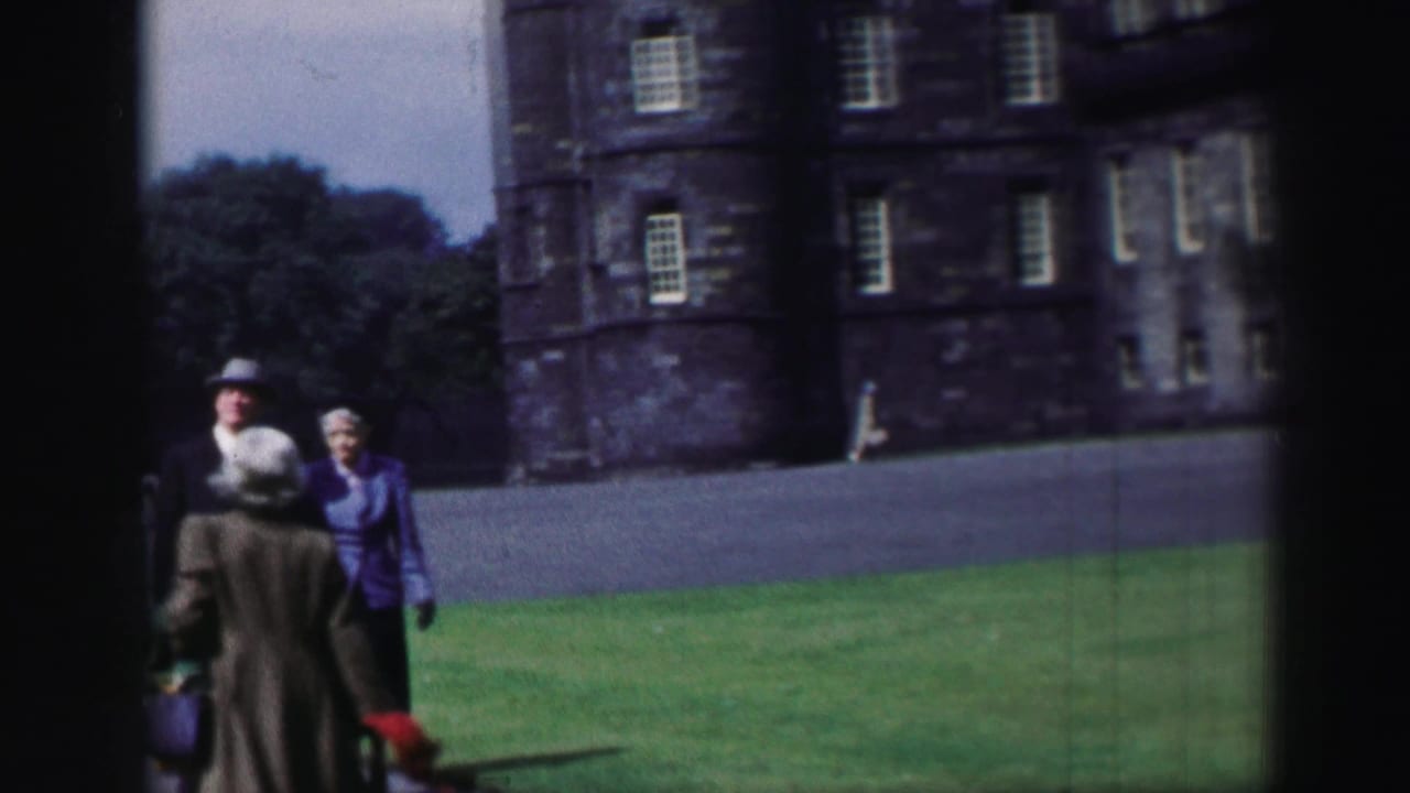 Man and woman walking on green castle grounds with a stone building behind them.