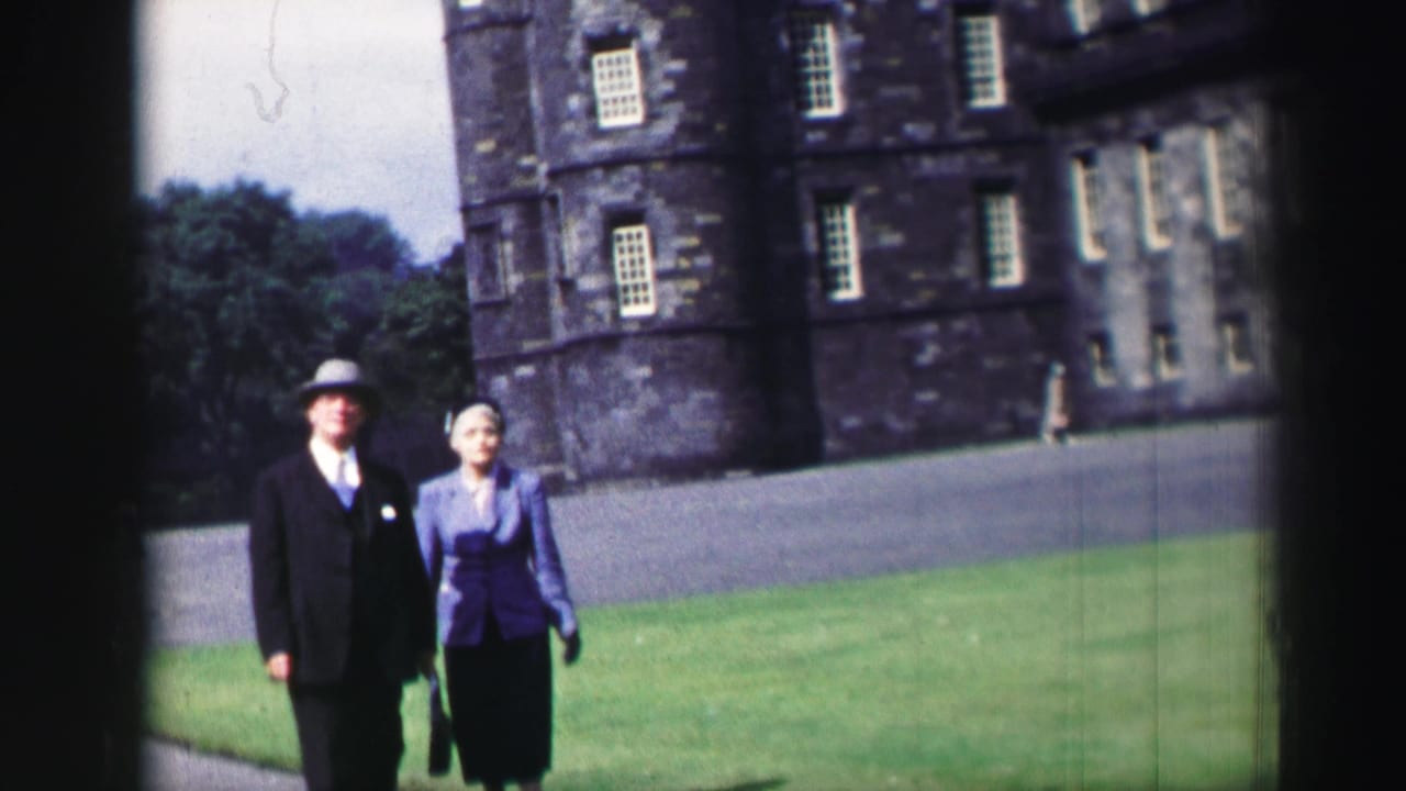 Man and woman walking on grass in front of a large stone castle.