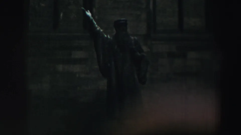 A dim 8mm frame shows a statue on the historic grounds, with the surrounding stone architecture falling into shadow.
