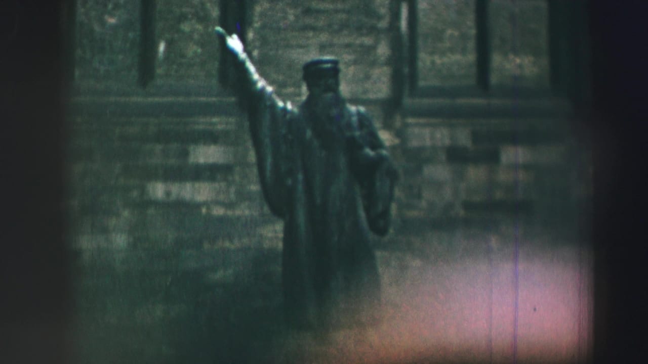 1952 8mm frame from Edinburgh showing a robed scholar-like statue with one arm raised before a stone facade.