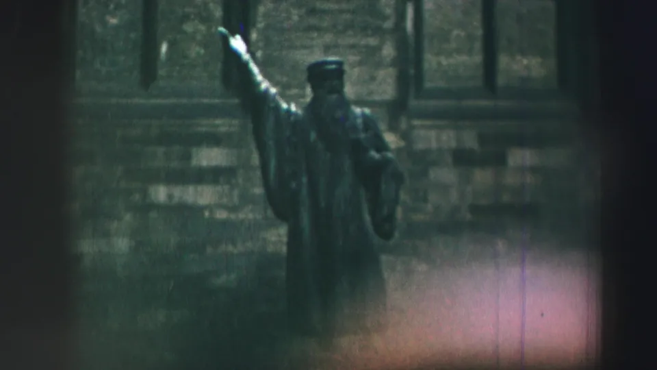 1952 8mm frame from Edinburgh showing a robed scholar-like statue with one arm raised before a stone facade.