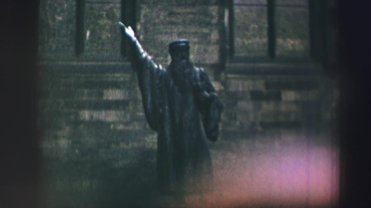 Raised-arm statue partly framed by dark film edges and a stone facade.
