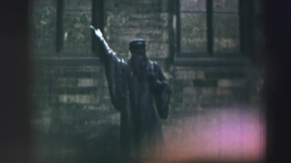 Soft 8mm frame showing the robed statue and raised arm more clearly against Edinburgh stonework.