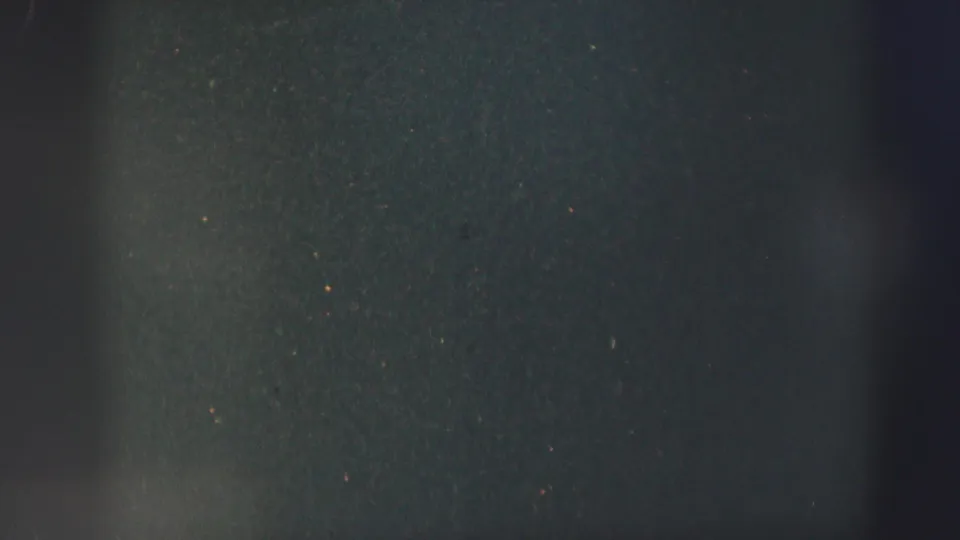 Late-frame 8mm texture from the 1952 clip, mostly dark and soft with visible dust, speckles, and vertical gate shadow.