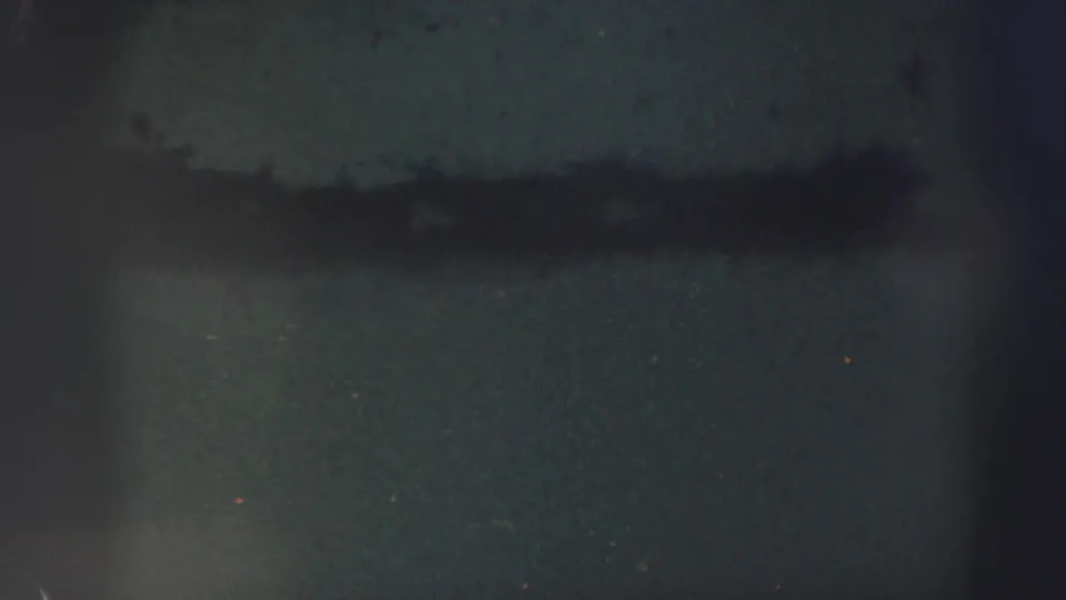 End of the 1952 Edinburgh 8mm clip showing dark, blurred film texture with a horizontal band, dust, and gate-edge shadows.