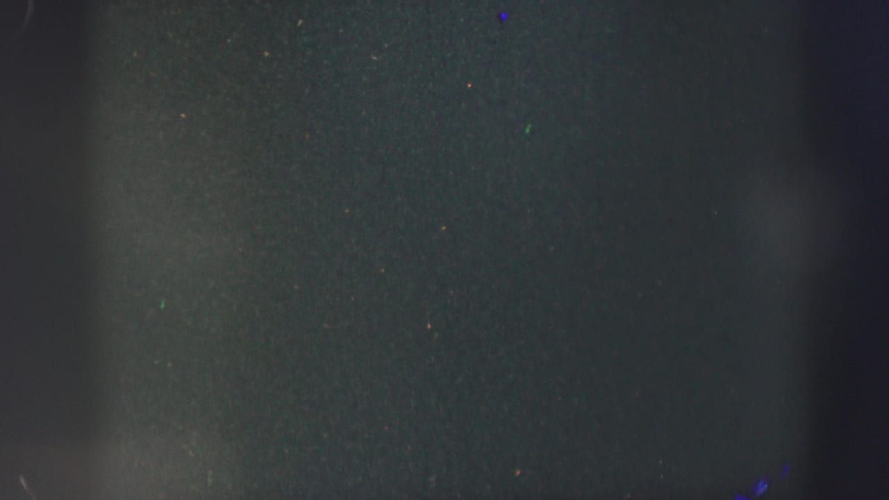 Mostly dark frame with partial purple fabric and faint film grain visible.