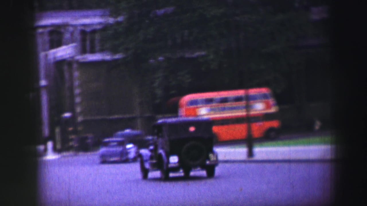 Vintage cars and a red double-decker bus moving along a broad city street.