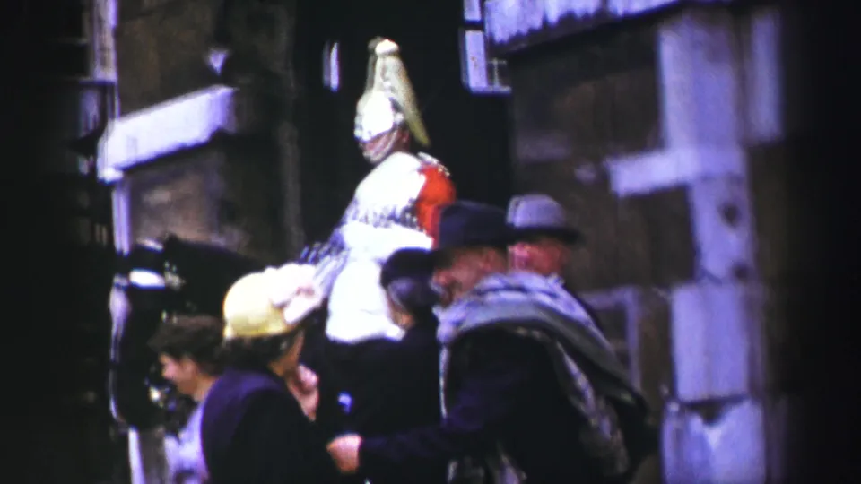 Closer street view of a mounted ceremonial soldier, dark horse, and pedestrians in period hats and coats in 1952 Edinburgh footage.