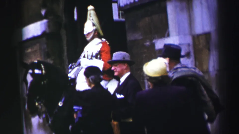 1952 Edinburgh home-movie frame showing a mounted ceremonial soldier, dark horse, and suited pedestrians near a stone building.