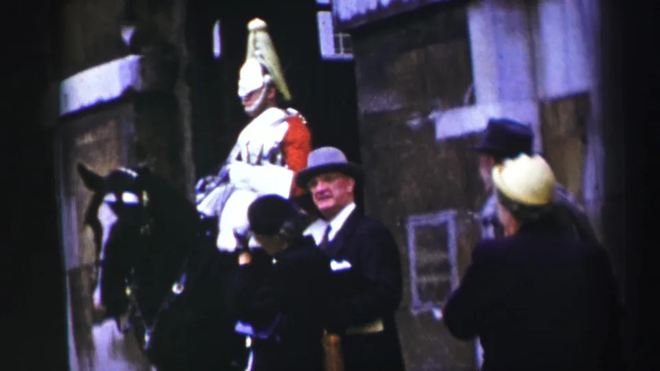 1952 Edinburgh home-movie frame showing a mounted royal guard in red uniform as visitors gather near the horse.