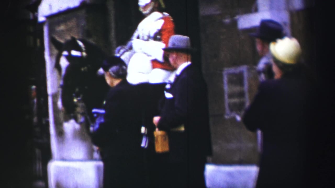The mounted guard remains near the stone building as civilians watch from close range in 1952 Edinburgh footage.