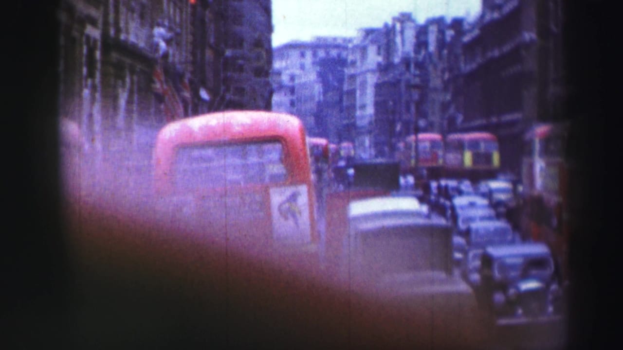 Handheld 1952 home-movie view of red double-decker buses, vintage cars, and tall city buildings in dense traffic.
