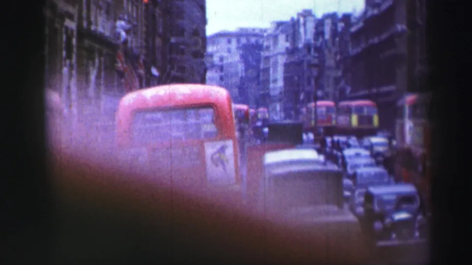 Handheld 1952 home-movie view of red double-decker buses, vintage cars, and tall city buildings in dense traffic.